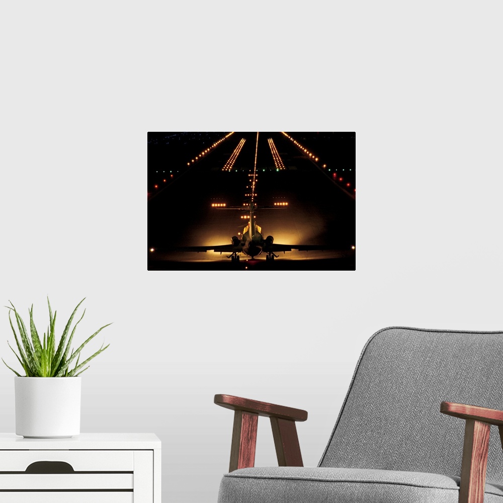 A modern room featuring Giant photograph shows a small aircraft stationed at the end of a brightly lit airstrip at nightt...