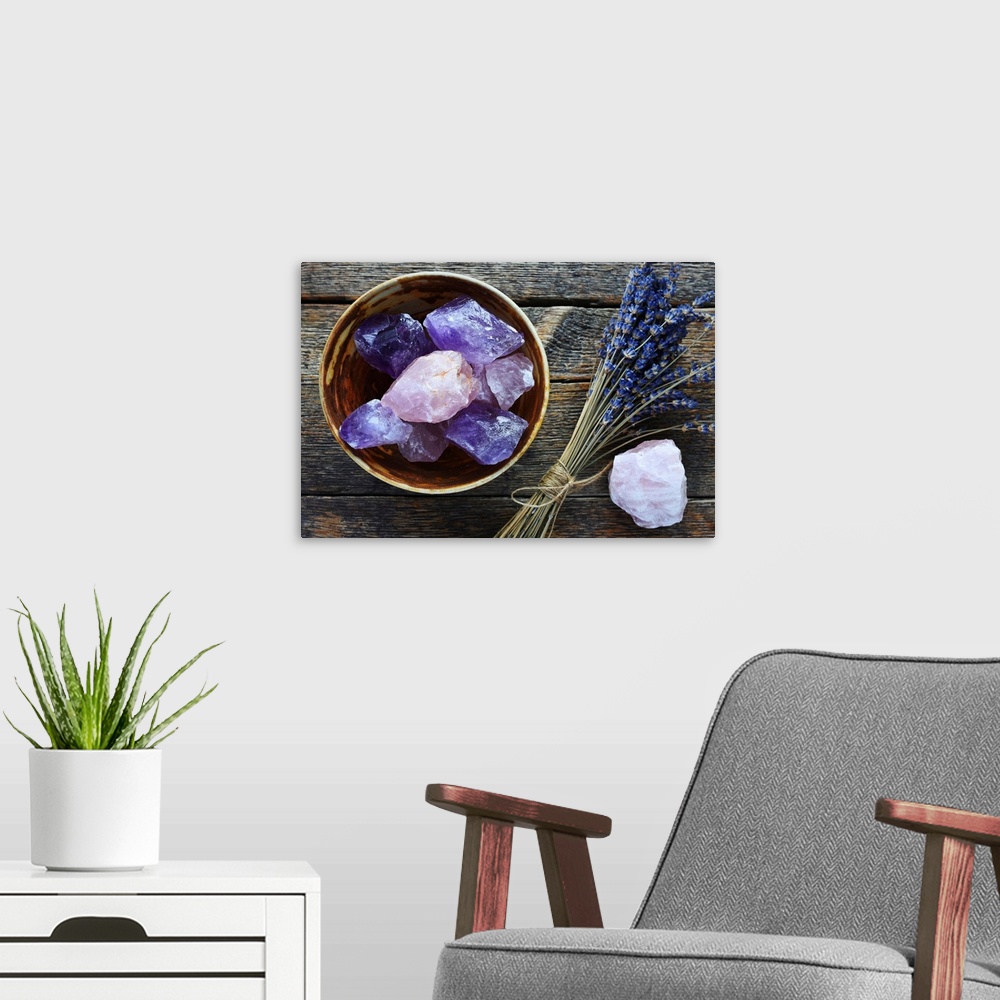A modern room featuring A table top image of a pottery bowl with large rose quartz and amethyst crystal with dried lavend...