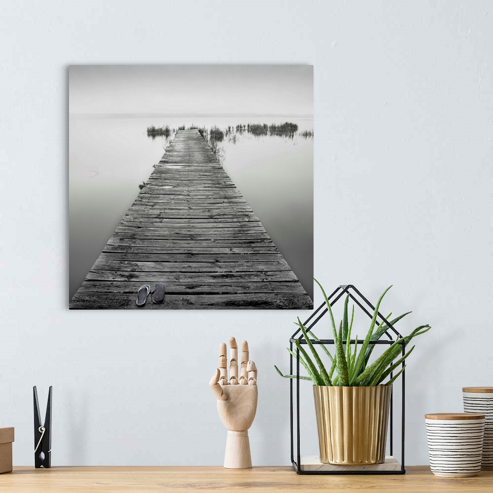 A bohemian room featuring An old wooden jetty on a very calm lake. A pair of shoes are also lying on the jetty.