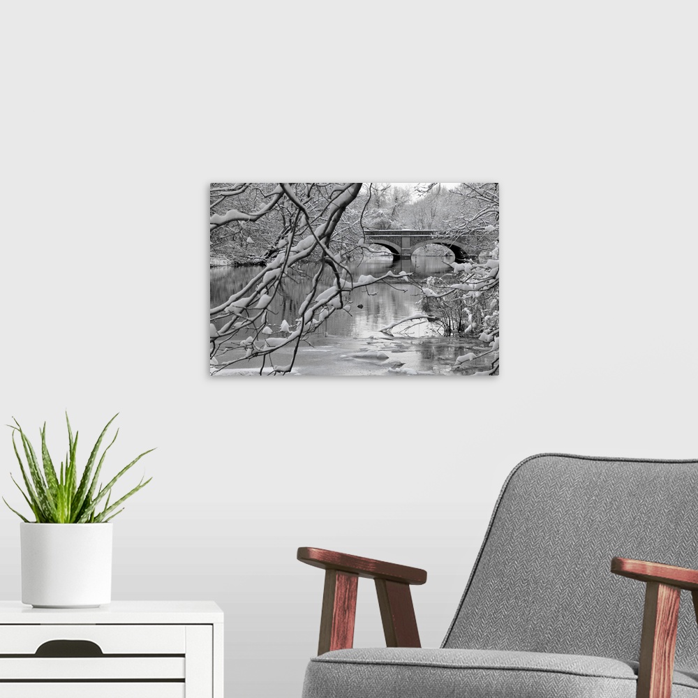 A modern room featuring Winter scene of arch bridge over partially frozen river seen trough snow covered branches.