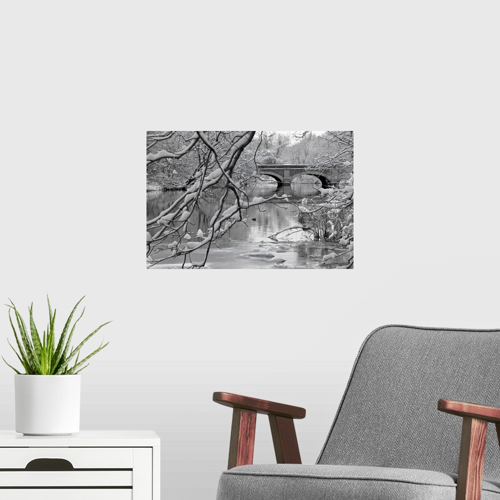 A modern room featuring Winter scene of arch bridge over partially frozen river seen trough snow covered branches.