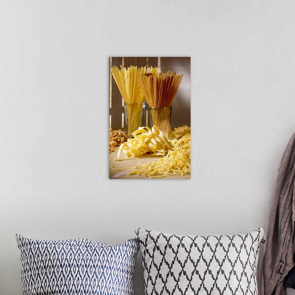 A bohemian room featuring Dry pasta in glass jars and fresh pasta scattered in front of it is photographed artistically.