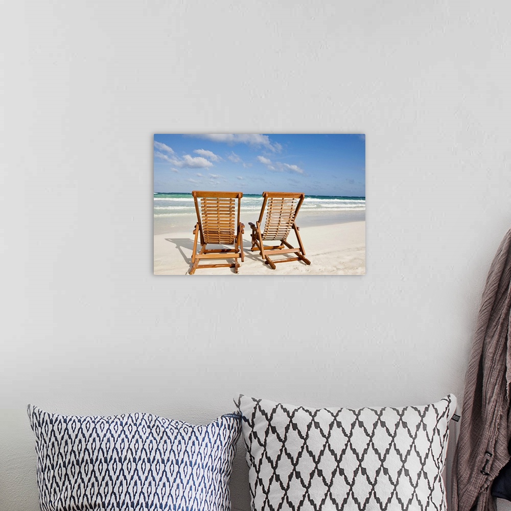 A bohemian room featuring Large landscape photograph of two wooden lounge chairs sitting on the beach, beneath a blue sky.