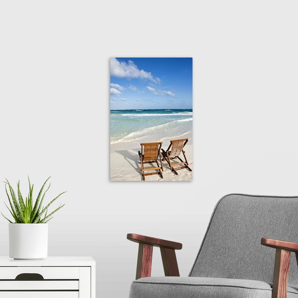 A modern room featuring Portrait photograph on a large wall hanging of two wooden lounge chairs on the beach, facing clea...