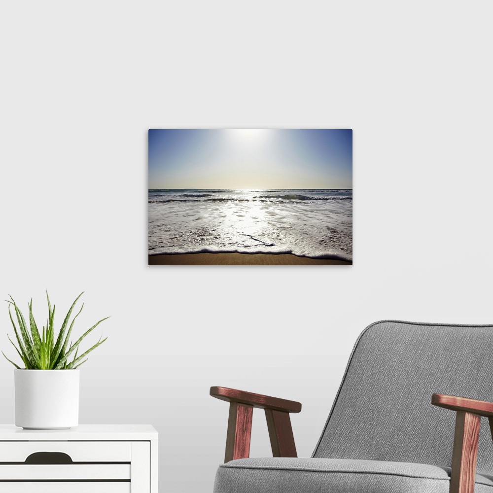 A modern room featuring Photograph of shoreline with sea spray and foam washing up under a bright clear sky.