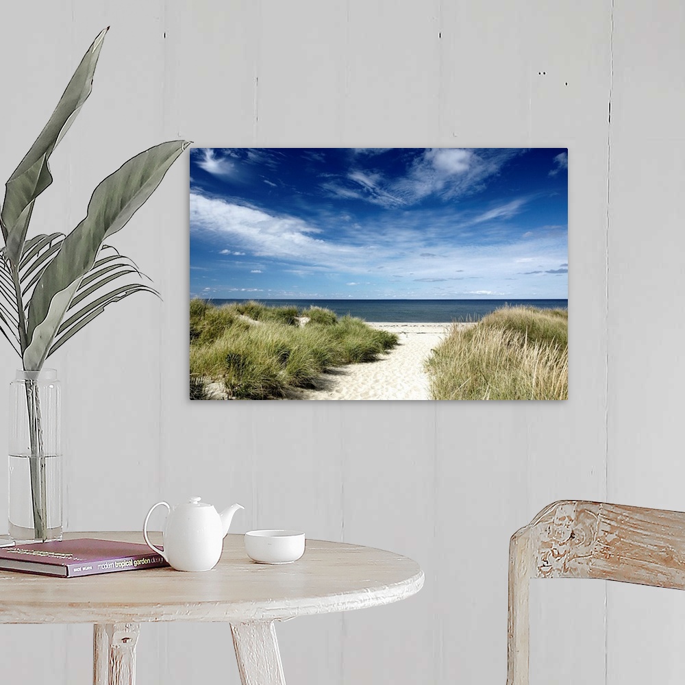 A farmhouse room featuring Photograph of sandy walkway lined by tall grass leading to a beach and calm ocean under cloudy sk...