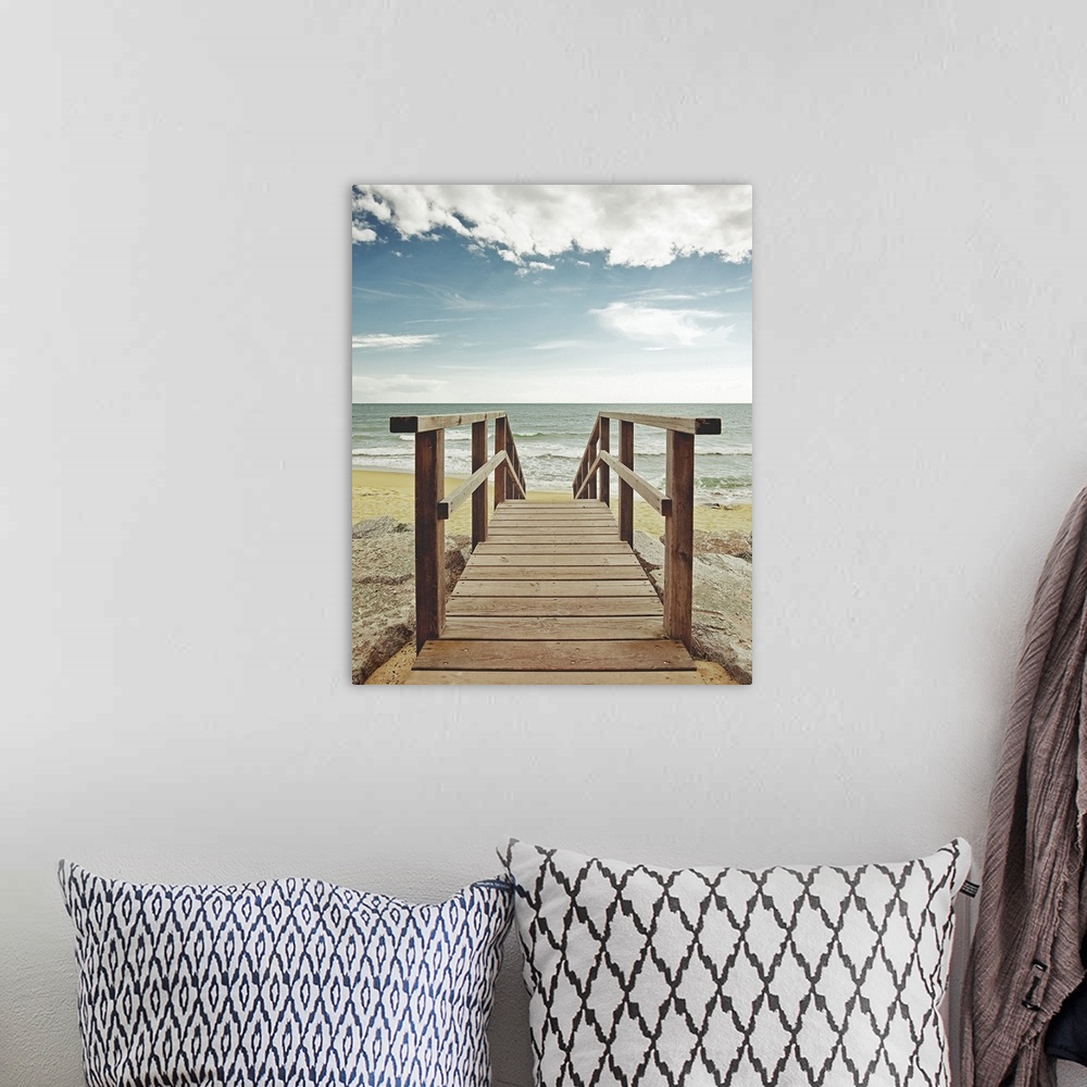 A bohemian room featuring Photograph looking straight on of a wooden bridge spanning over large rocks that lead to a sandy ...