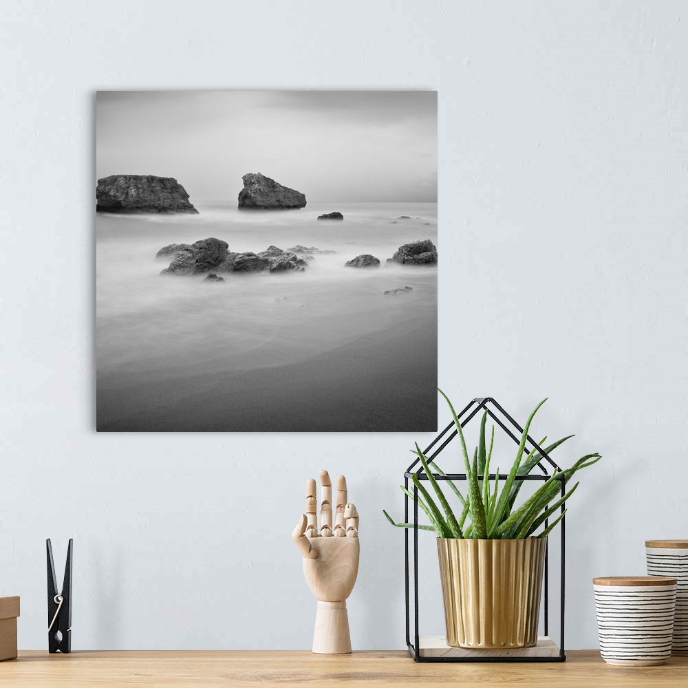 A bohemian room featuring Black and White image of rocks in the ocean near a sandy beach.