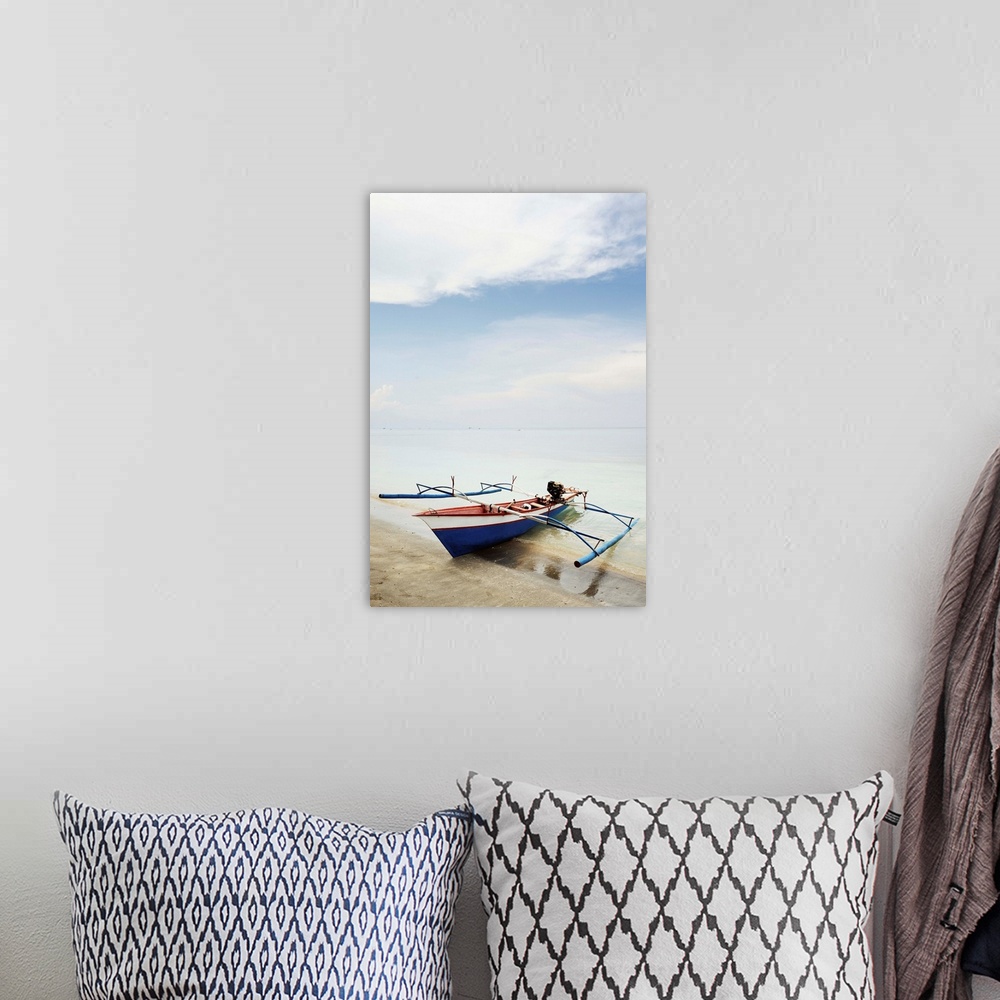 A bohemian room featuring Blue, red and white wooden outrigger fishing boat on sandy beach.