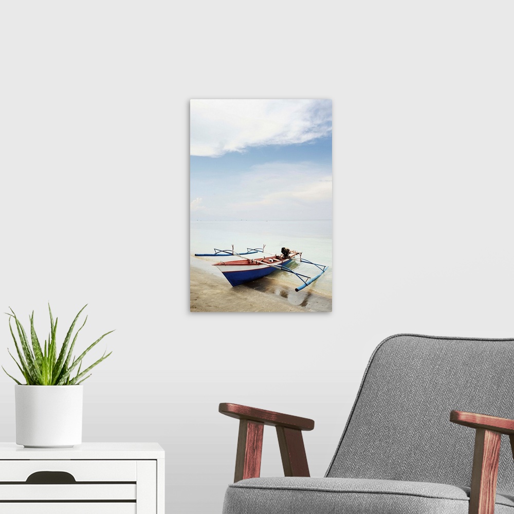 A modern room featuring Blue, red and white wooden outrigger fishing boat on sandy beach.