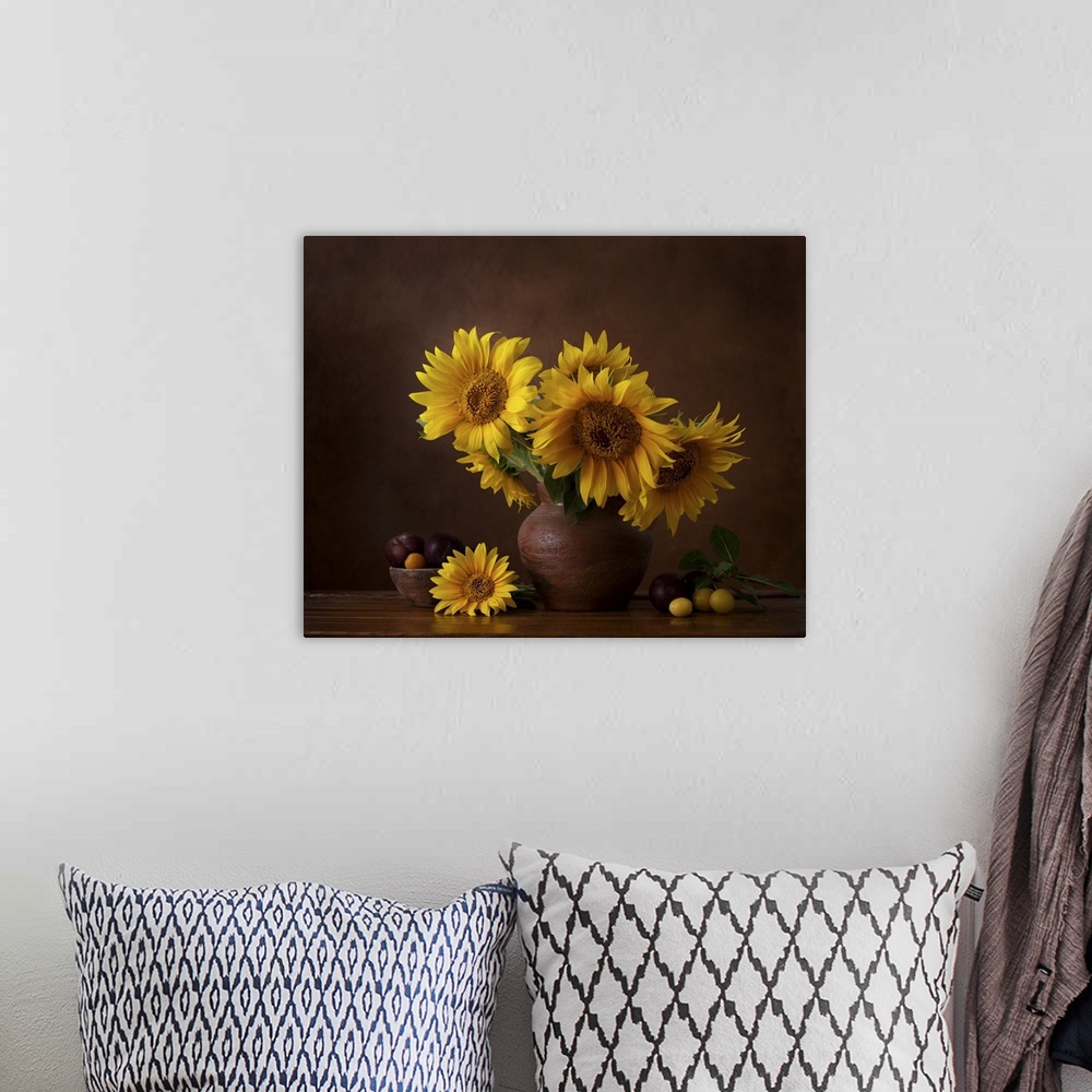 A bohemian room featuring Bouquet of sunflowers in old clay jug with ripe cherry plum branches in the foreground.