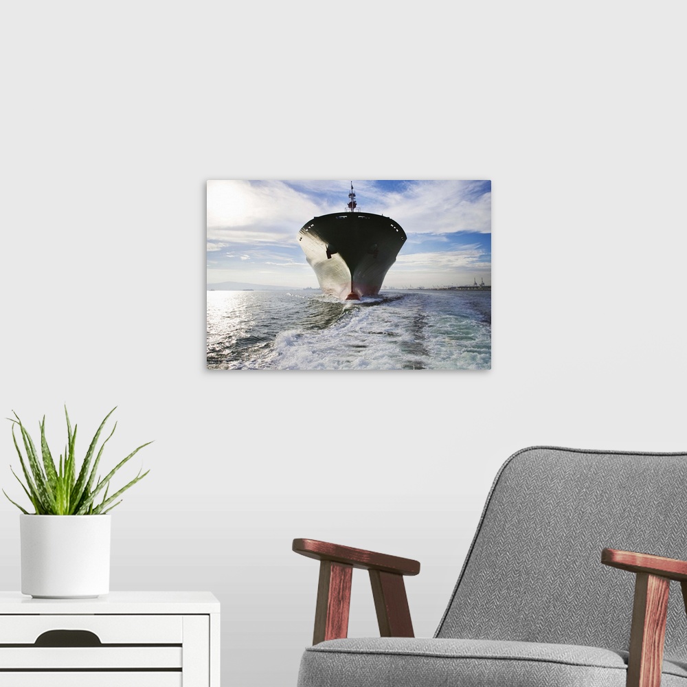 A modern room featuring Bow view of cargo ship sailing out of port.