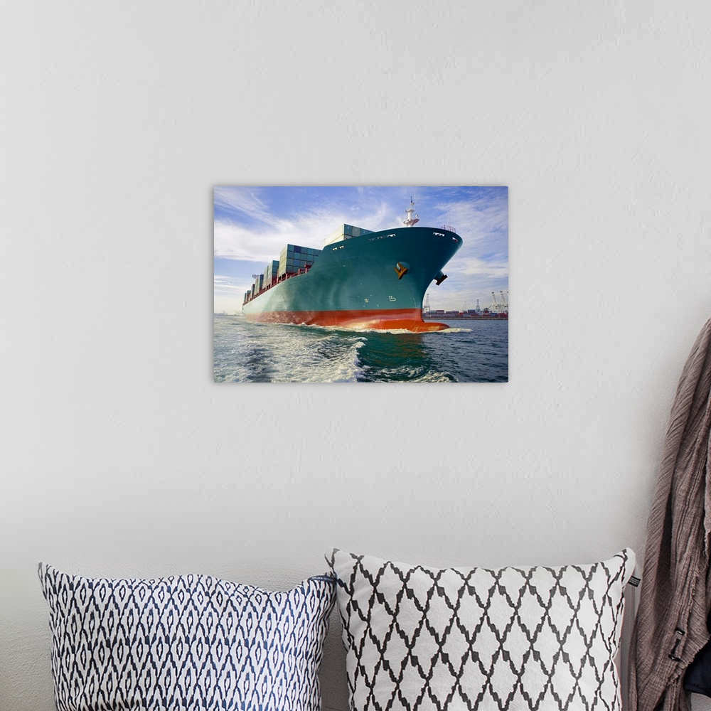 A bohemian room featuring This oversized photograph is taken while looking up at a large cargo ship that is headed out to sea.