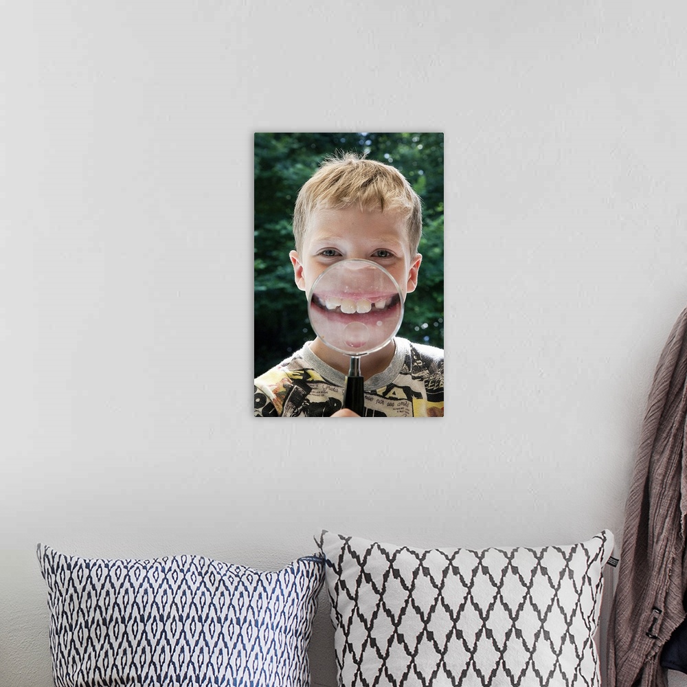 A bohemian room featuring blond boy behind magnifying glass smiling