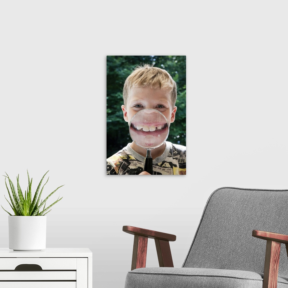 A modern room featuring blond boy behind magnifying glass smiling