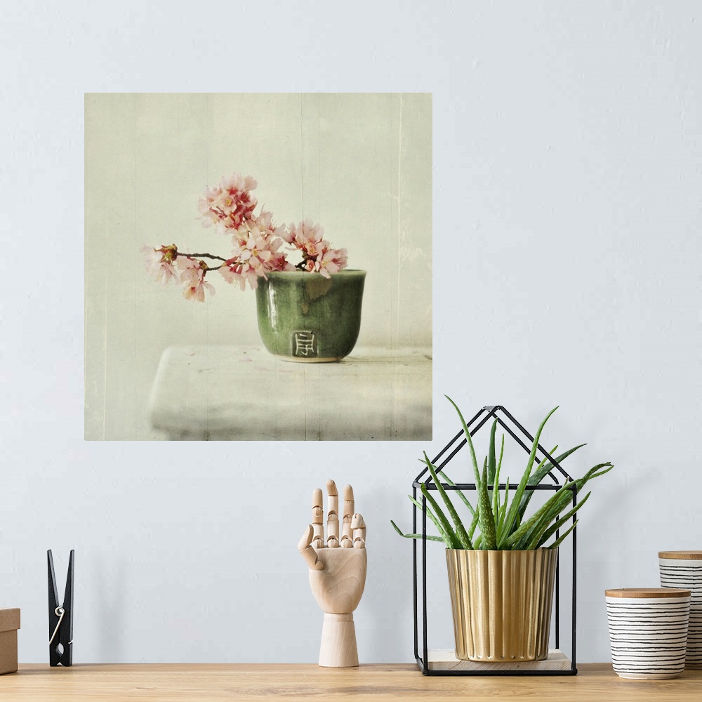 A bohemian room featuring Branch of cherry blossoms sit in green tea bowl on white table.