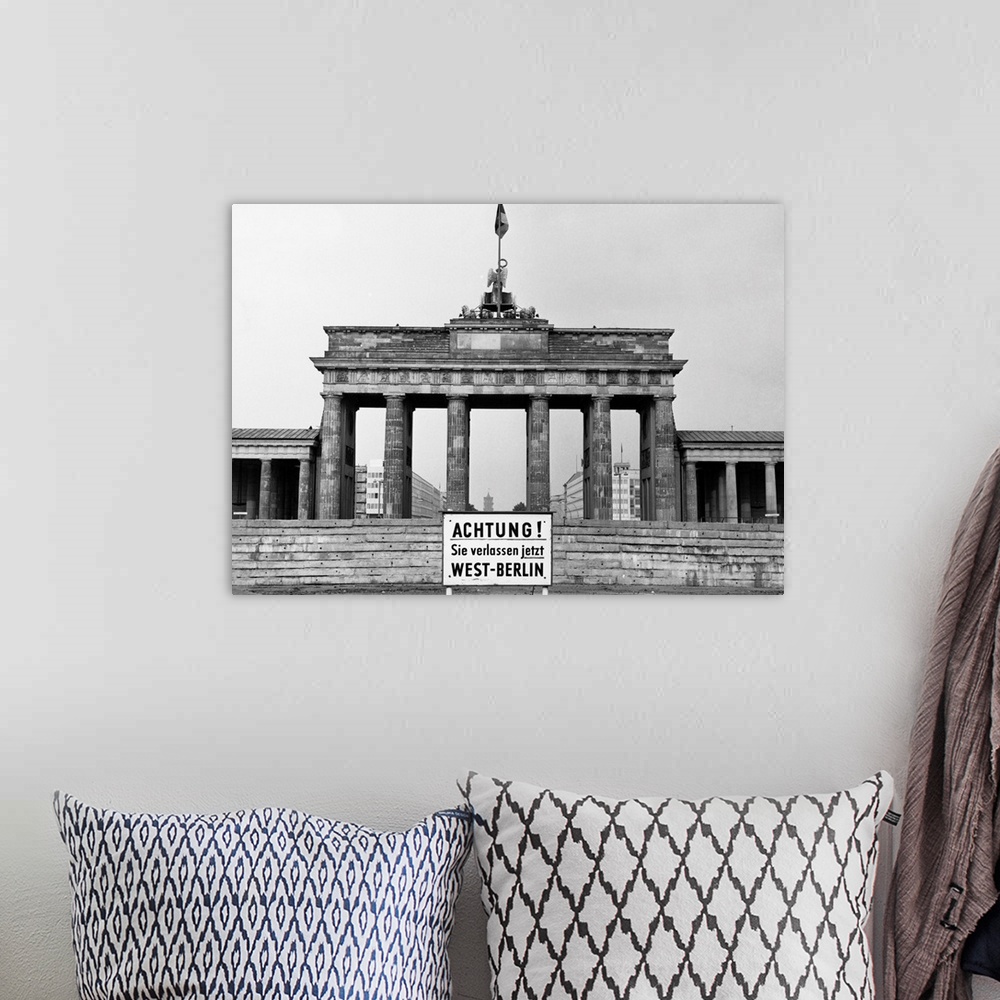A bohemian room featuring The Brandenburg Gate in East Berlin. In front, a sign in German warns of the impending border bet...