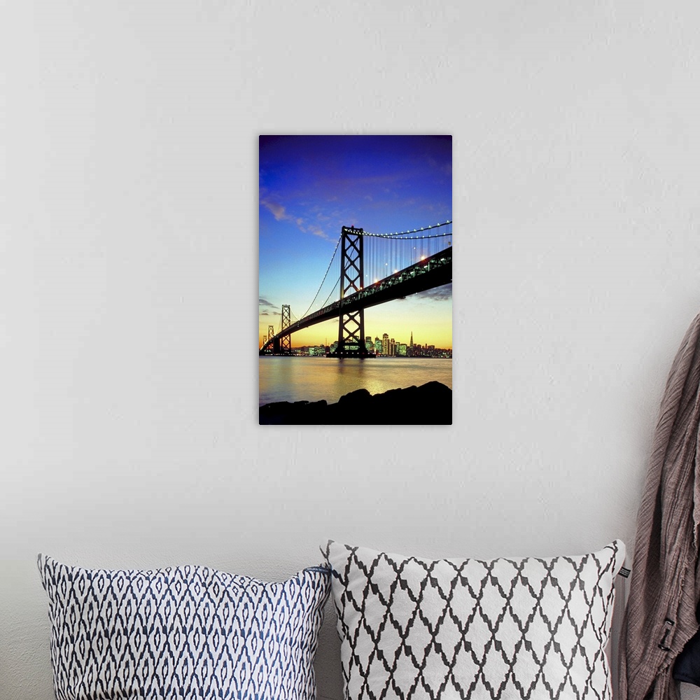 A bohemian room featuring The bay bridge is silhouetted under a sunset sky with the skyline in the distance lit up.