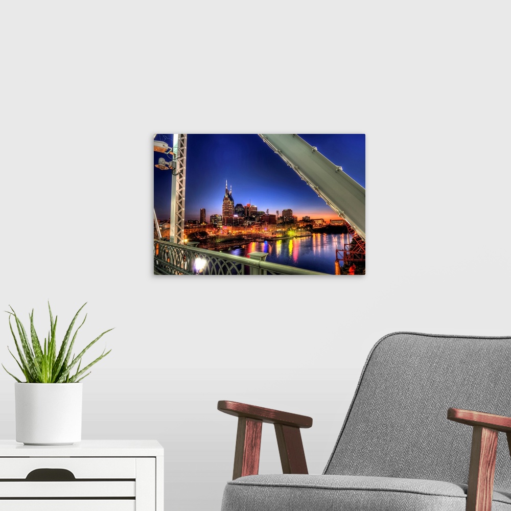 A modern room featuring Large wall docor overlooking a lit up downtown cityscape from a bridge at dusk with a river runni...