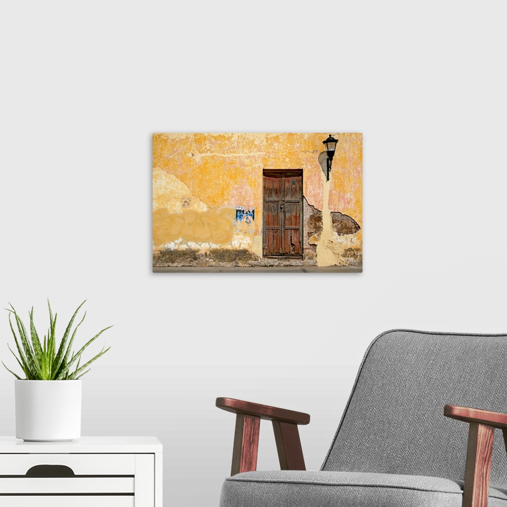 A modern room featuring An old cracked wooden door on a bright yellow wall with crumbling stucco on a street in San Crist...