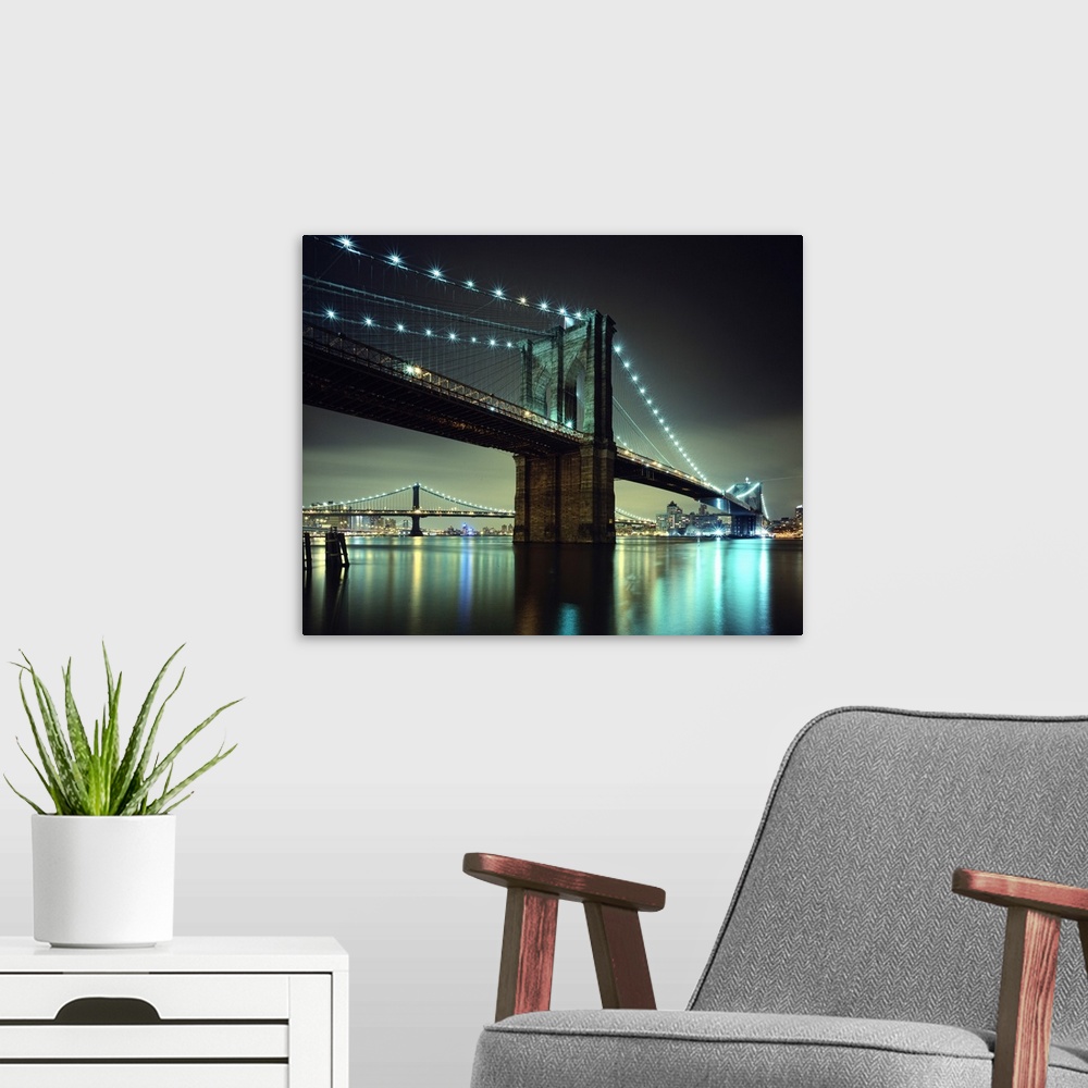 A modern room featuring Horizontal photograph on a large wall hanging of the Brooklyn Bridge at night, the  Manhattan Bri...