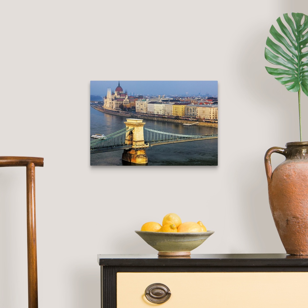 A traditional room featuring Warm sunlight spotlights the Chain Bridge and the Hungarian Parliament Building against a blue sk...