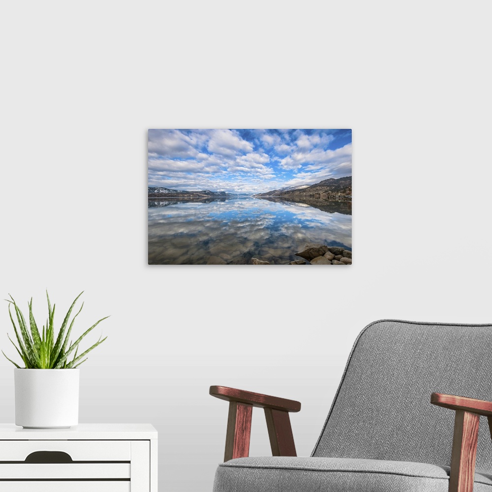 A modern room featuring Late winter reflections of surrounding mountains and scattered clouds are mirrored in Okanagan lake.