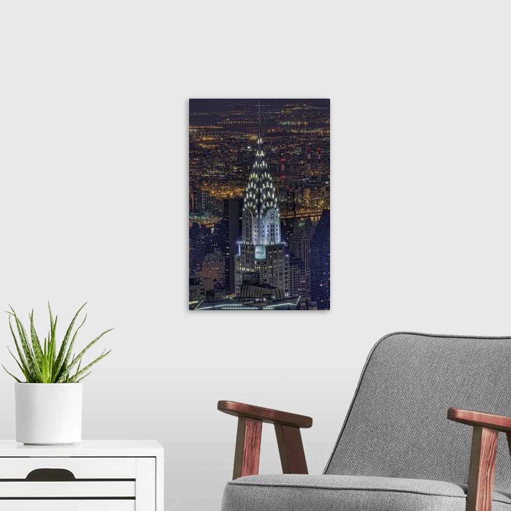 A modern room featuring Aerial vertical picture of the top of the Chrysler building lit up at night with the rest of down...