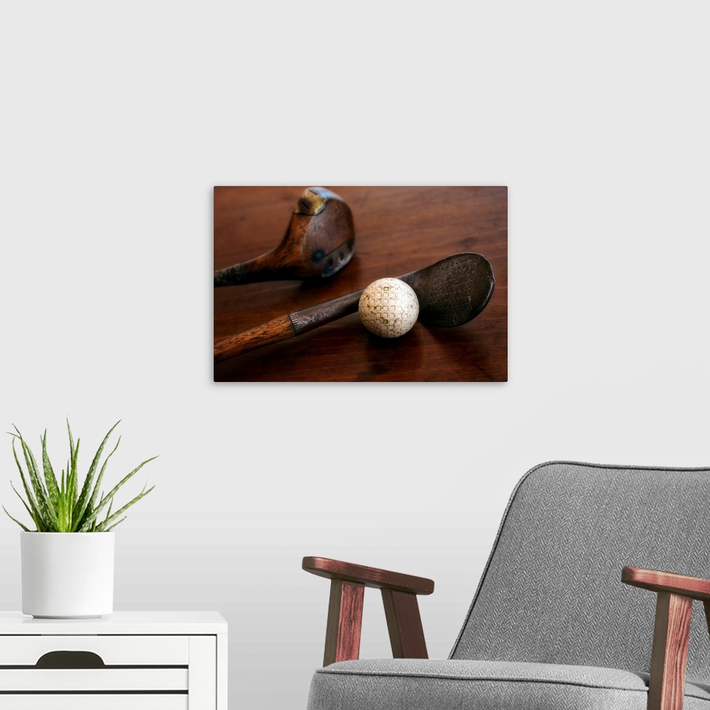 A modern room featuring Horizontal photograph on a large canvas of two antique golf clubs and a ball, lying on a wooden t...
