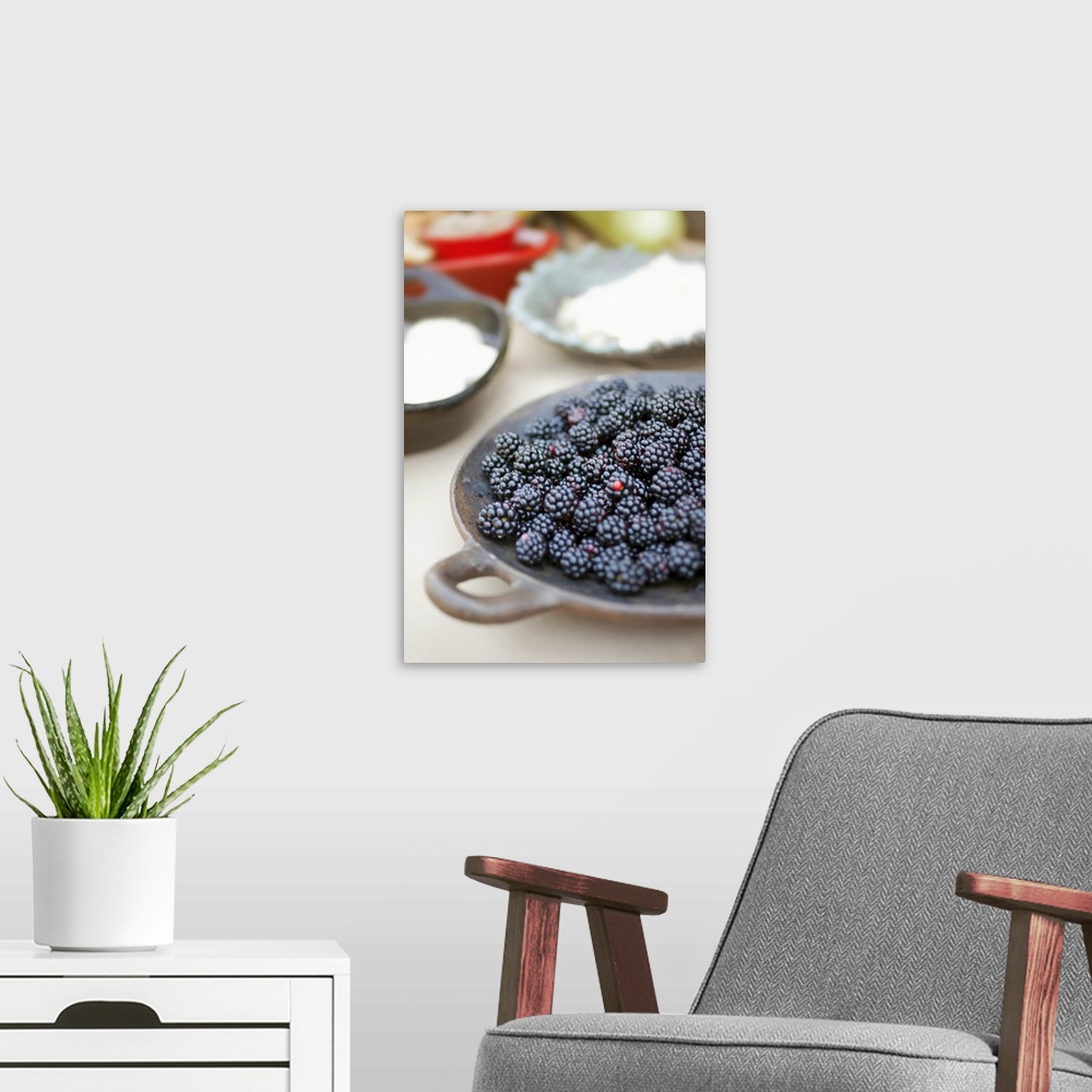 A modern room featuring Close up of bowl of blackberries on a table with bowls of cheese and breads in the background.
