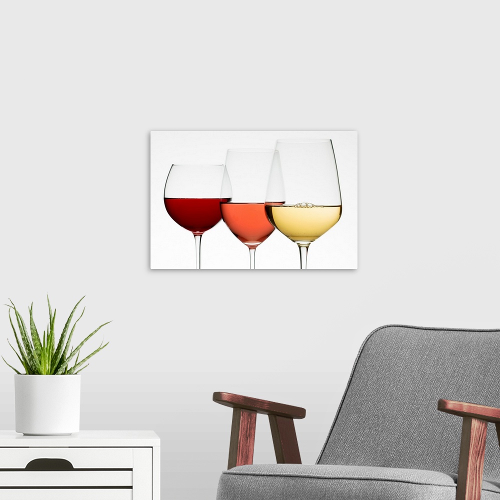 A modern room featuring Three different wine glasses stand next to each other all filled with different types of wine.