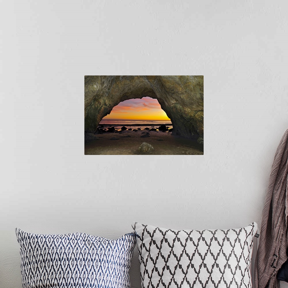 A bohemian room featuring Dramatic sunset seen from inside cave on beach.