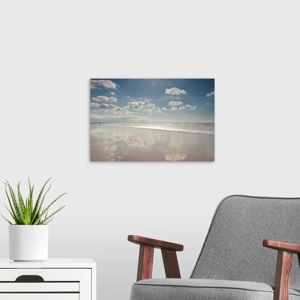 A modern room featuring Empty beach with a thin film of water reflecting fluffy clouds in a sunny blue sky.