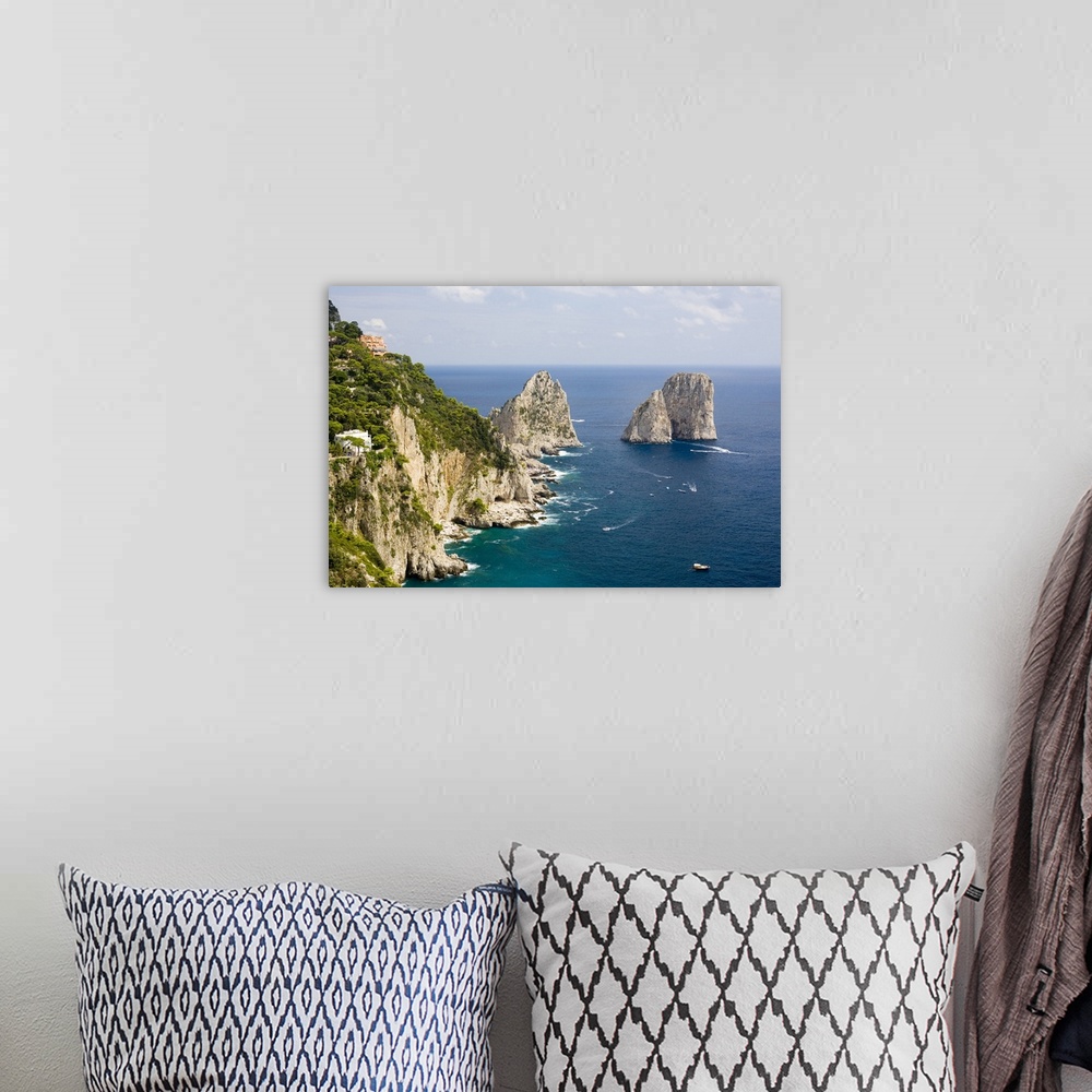 A bohemian room featuring Large rock formations stand in the water next to an immense cliff off the Italian coast.