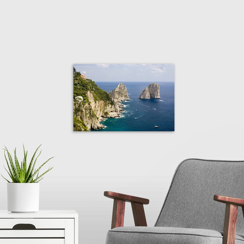 A modern room featuring Large rock formations stand in the water next to an immense cliff off the Italian coast.