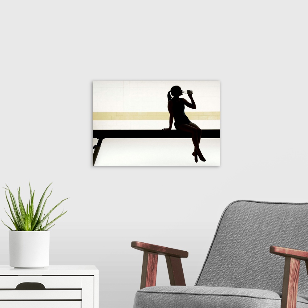 A modern room featuring Female gymnast sitting on balance beam drinking water