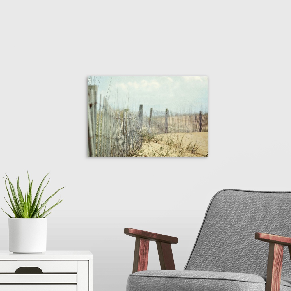 A modern room featuring Photograph of wooden fence and tall grass on hills of sand at the coast under cloudy skies.
