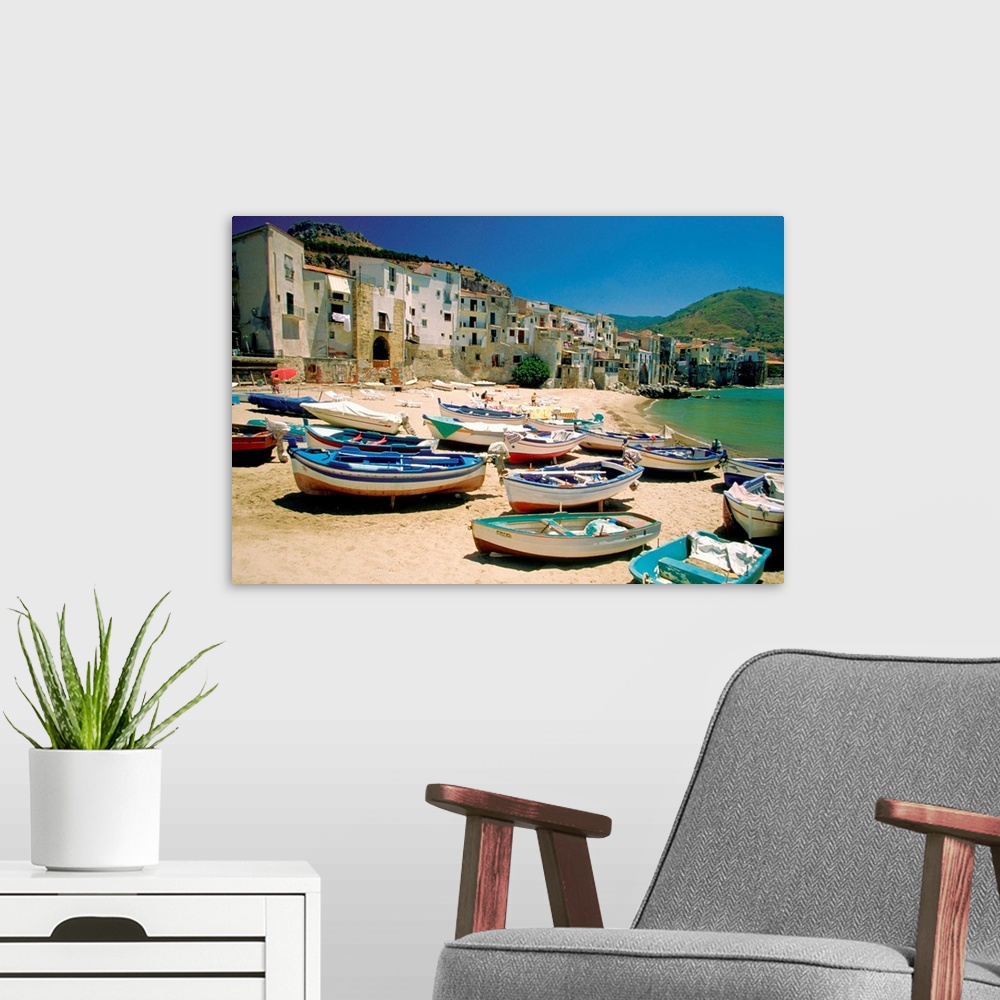 A modern room featuring Huge photograph showcases a fleet of small water vessels sitting on top of a sandy beach within t...