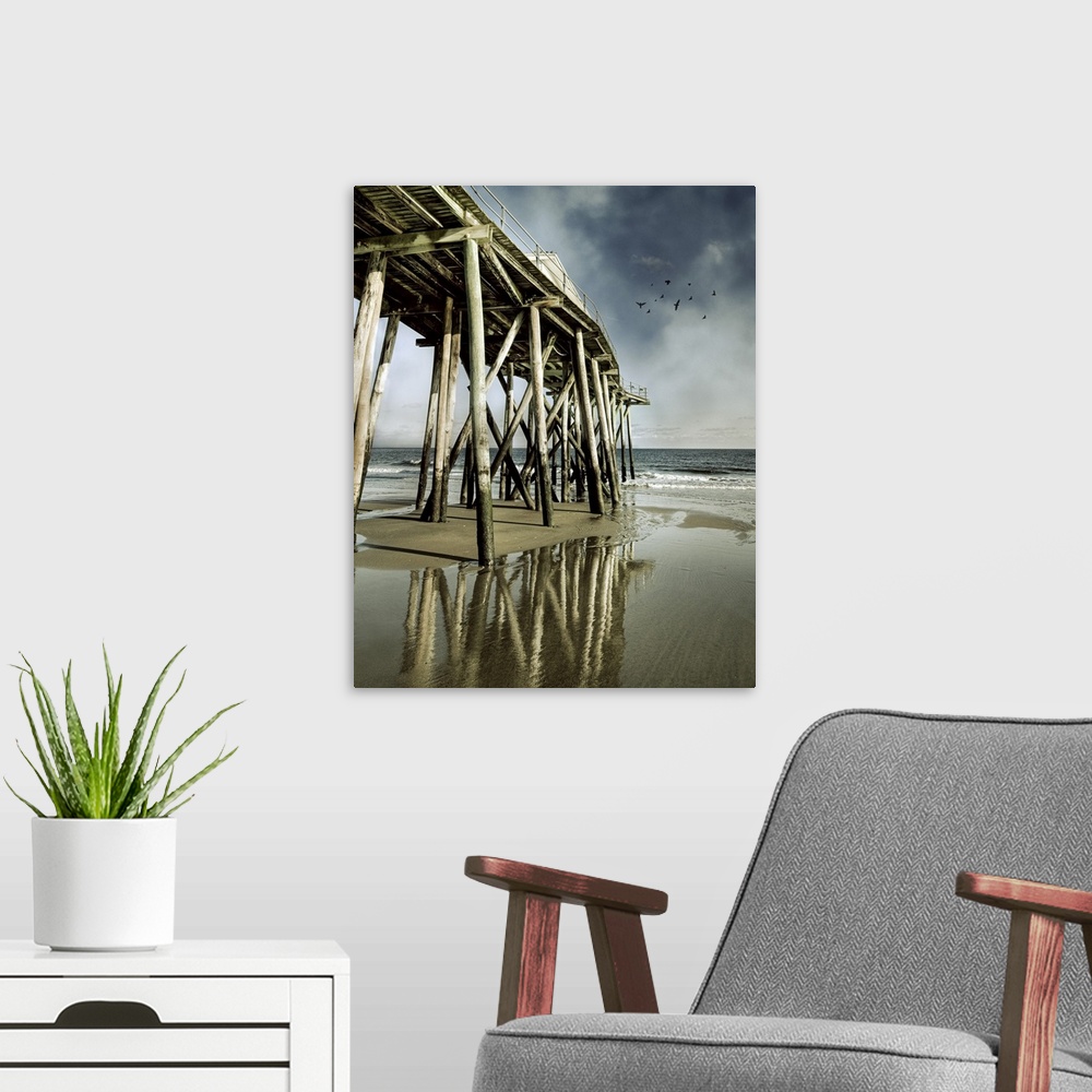 A modern room featuring Fishing shack pier with reflection in sea and flock of birds in sky.