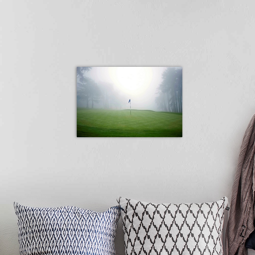A bohemian room featuring Flag on putting green on golf course, fog and trees in background