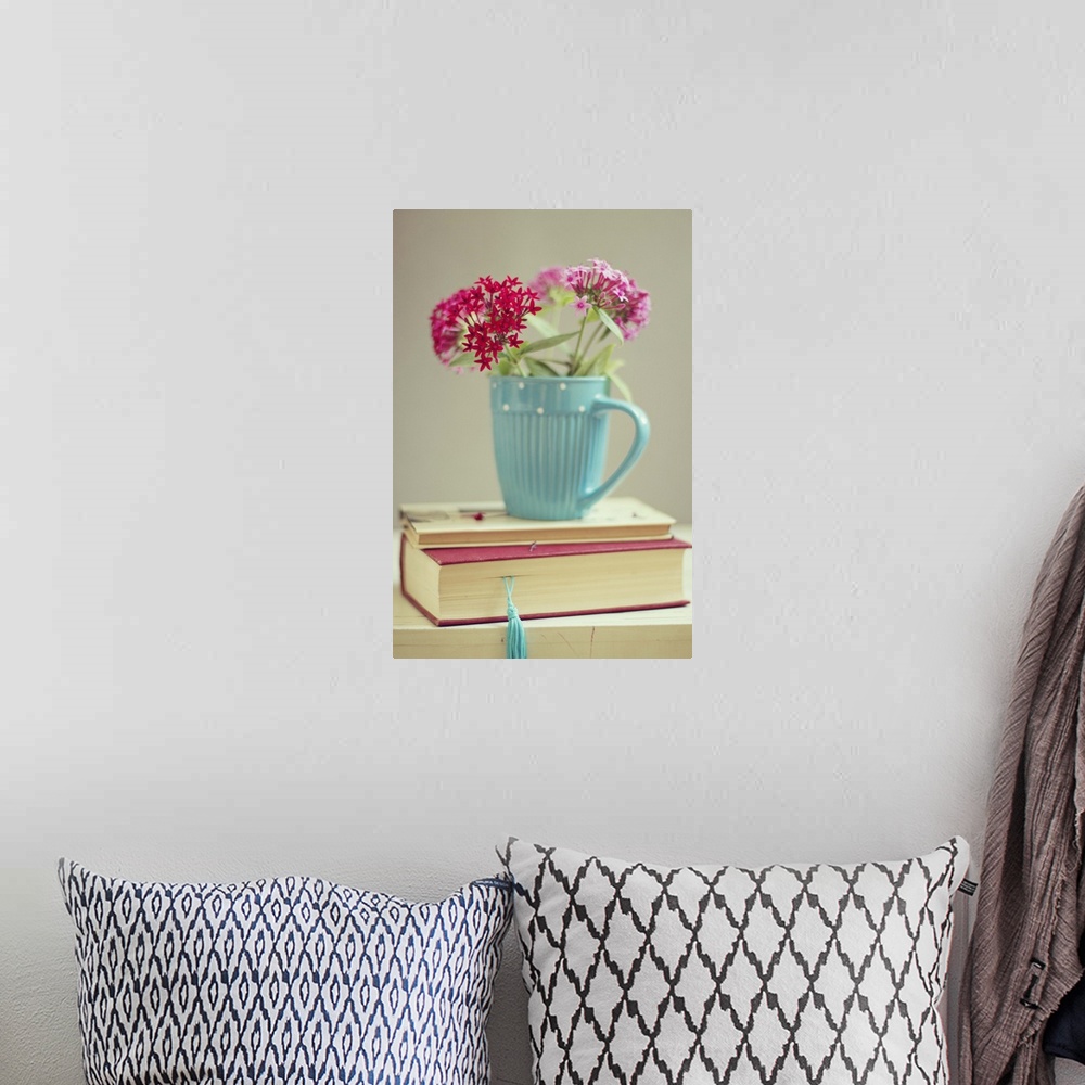 A bohemian room featuring Flowers in blue cup on two books.