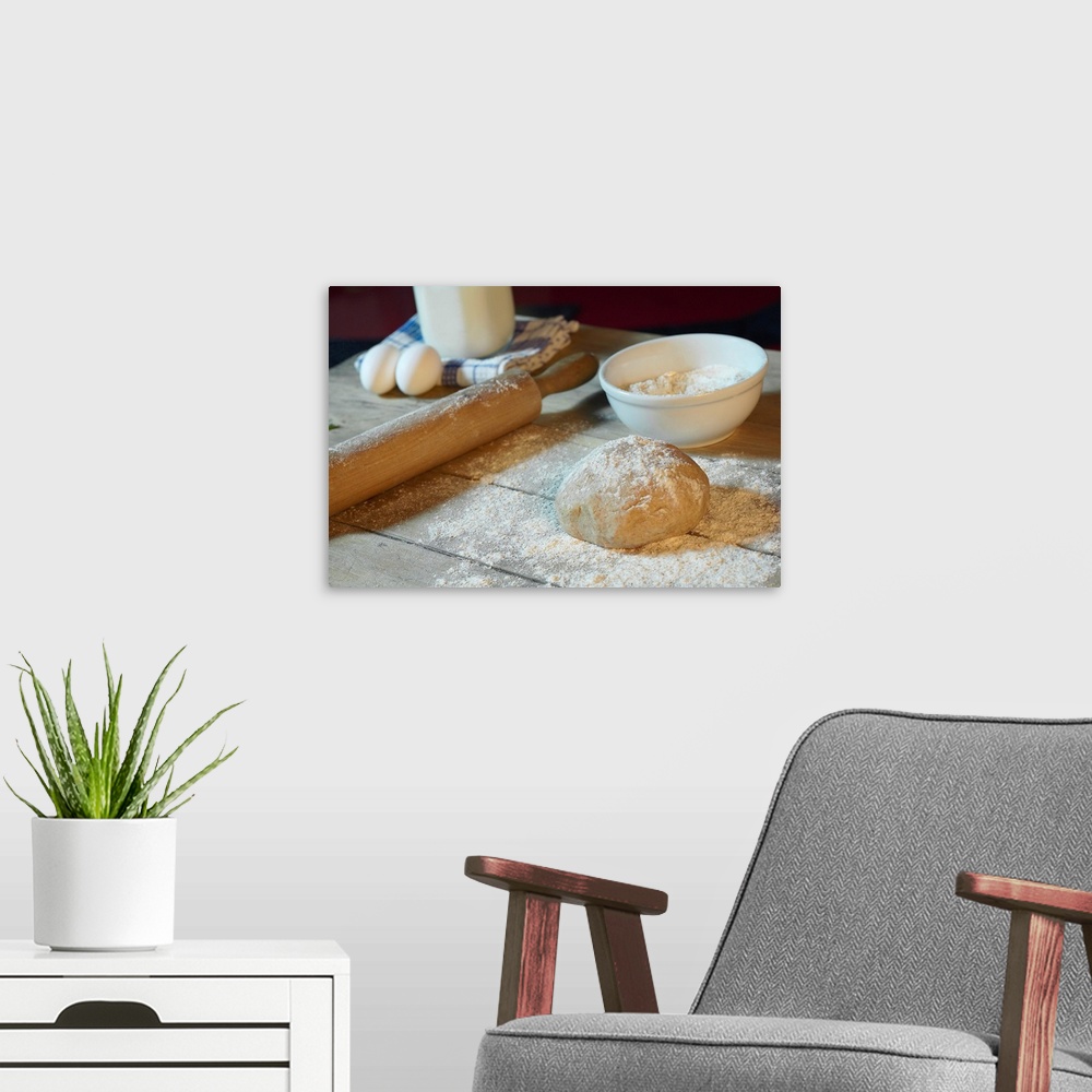A modern room featuring Large horizontal photograph of bread dough in ball on a wooden table, sprinkled with flour.  Obje...