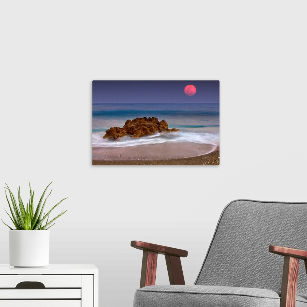 A modern room featuring A unique rock formation sits in the ocean water which is photographed under a deep red moon.