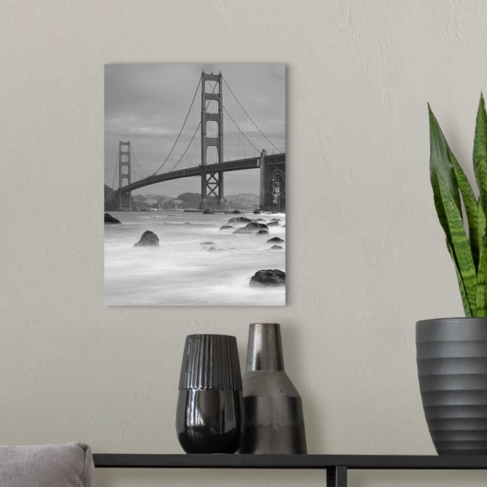 A modern room featuring Photo on canvas of the Golden Gate Bridge with wave breaking through rocks in the water.