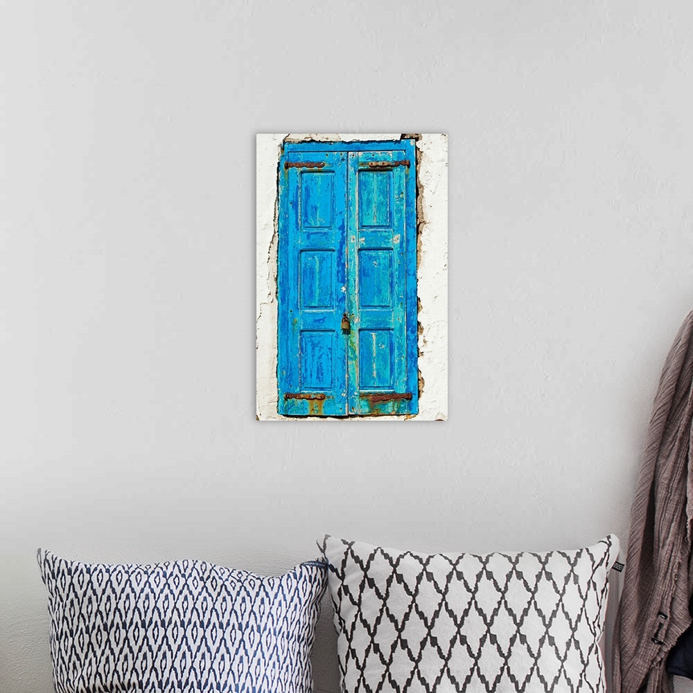 A bohemian room featuring Rustic, paint peeling blue door in the middle of the white side of a home.