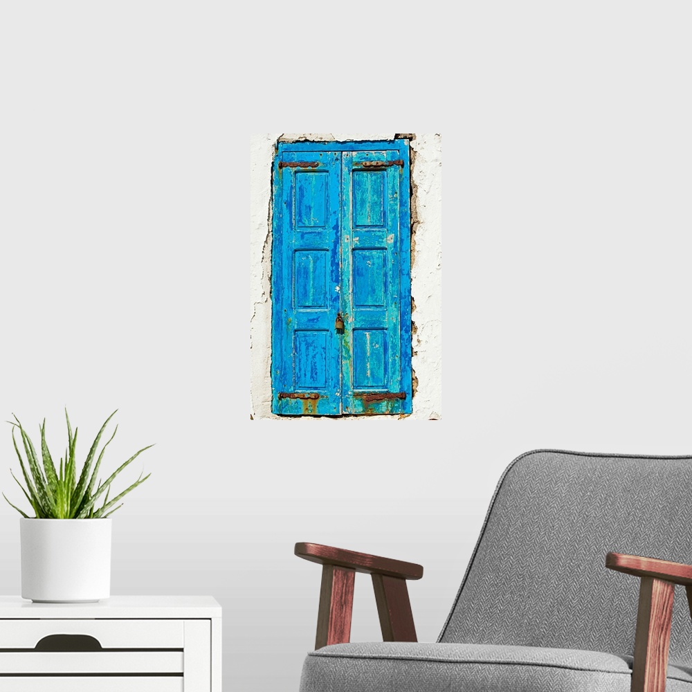 A modern room featuring Rustic, paint peeling blue door in the middle of the white side of a home.