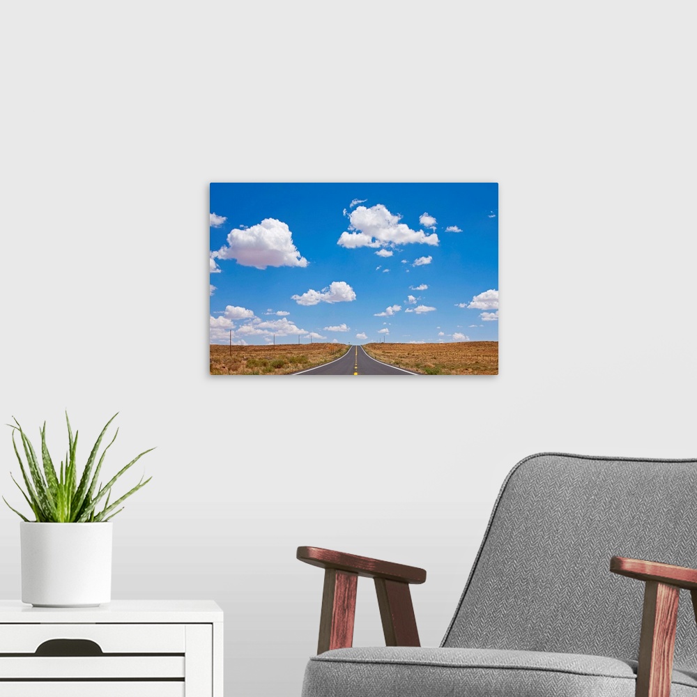 A modern room featuring Cumulus clouds above empty US 87 highway in desert on summer morning.