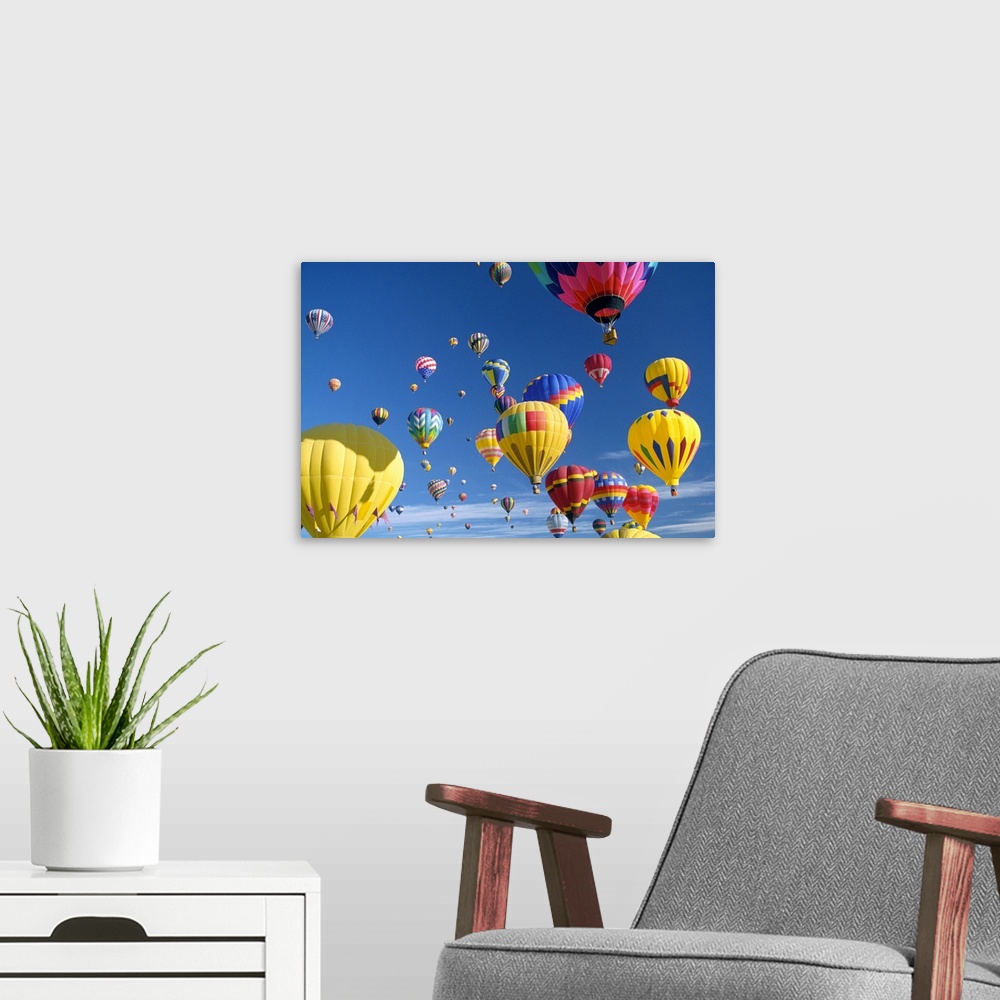A modern room featuring Big, horizontal photograph of many brightly colored hot air balloons with varying patterns, float...