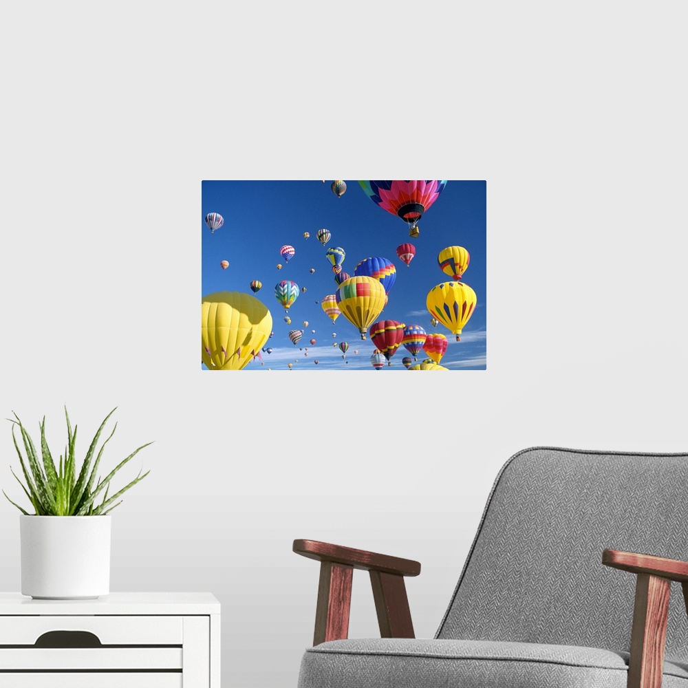 A modern room featuring Big, horizontal photograph of many brightly colored hot air balloons with varying patterns, float...