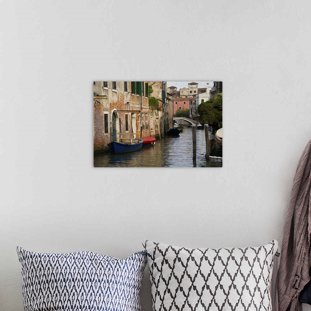A bohemian room featuring A picture of a canal is taken with boats docked on the left side where buildings line the water.